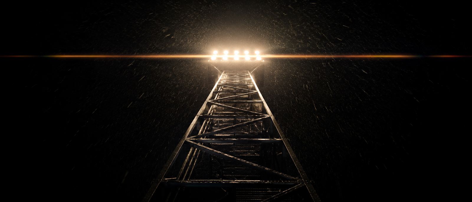 Stadium floodlight tower shot from below at night with rain streaking through the beams